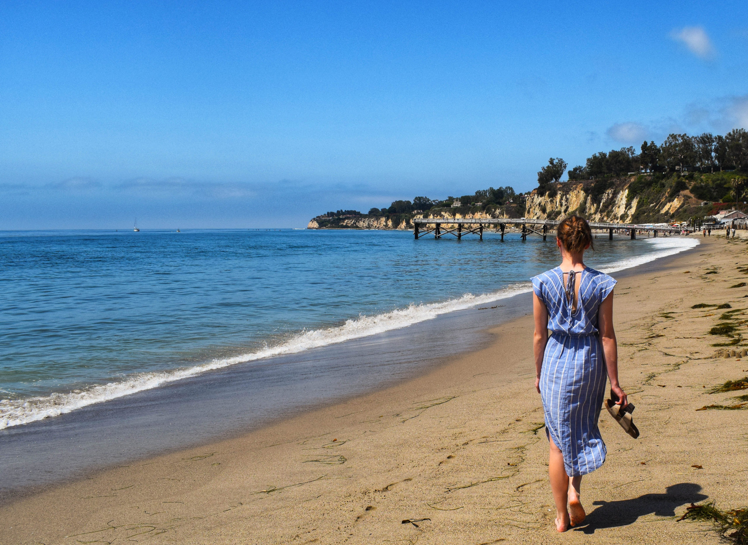 Woman walking on the beach in a blue dress in Malibu by the ocean